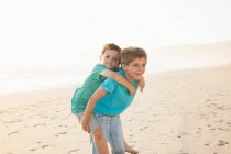 Menino dando irmão piggyback no praia — Fotografia de Stock