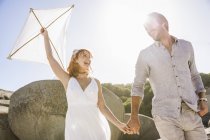 Low angle view of couple holding hands, holding kite face to face smiling — Stock Photo