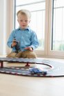 Мальчик играет с игрушечными гоночными машинами на полу гостиной — стоковое фото