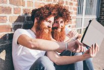 Young male hipster twins with red hair and beards browsing digital tablet on sidewalk — Stock Photo