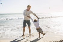 Padre e hijo en la playa tomados de la mano remando - foto de stock