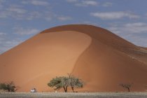 Camión de cuatro ruedas estacionado en la base de una duna de arena gigante, Parque Nacional Sossusvlei, Namibia - foto de stock