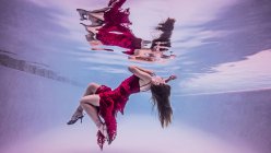 Vista subacquea della ragazza che indossa abito rosso e scarpe con tacco alto, galleggiante verso la superficie dell'acqua — Foto stock