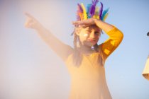 Chica vestida como nativa americana en tocado de plumas con la mano sombreando los ojos señalando - foto de stock