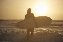 Силует молоді чоловіки surfer проведення серфінгу в море, Девон, Англія, Великобританія — стокове фото