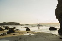 Uomo maturo che cammina verso il mare, tenendo tavola da surf — Foto stock