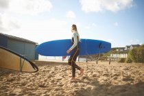 Femme surfeuse sur la plage, portant une planche de surf — Photo de stock