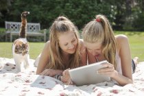 Two teenage girls looking at digital tablet on picnic blanket — Stock Photo
