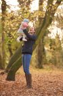 Mid adult woman holding up baby daughter in autumn park — Stock Photo