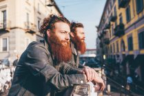 Young male hipster twins with red hair and beards looking out from city footbridge — Stock Photo