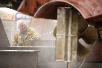 Senior männlicher Schiffsmaler reinigt Schiffsrumpf mit Hochdruckreiniger in Schiffsmaler-Werft — Stockfoto