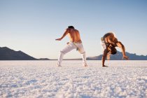Vista a nivel de superficie de dos hombres realizando capoeira en Bonneville Salt Flats, Utah, EE.UU. - foto de stock