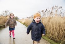 Petite sœur et frère courent le long de la route rurale — Photo de stock