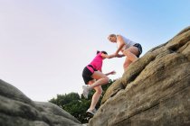 Дві молоді жінки-бігуни допомагають один одному на вершині формування каменю — стокове фото