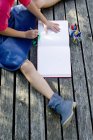 Girl drawing picture in album while sitting on boardwalk — Stock Photo