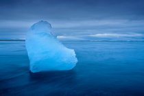 Айсберг плавает в ледниковых водах с облачным небом — стоковое фото