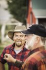Farmers wearing plaid shirts chatting on farmland — Stock Photo