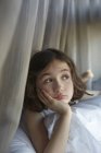 Menina reclinada na cama olhando para os lados — Fotografia de Stock