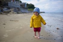 Baby girl on beach wearing sunhat and raincoat — Stock Photo