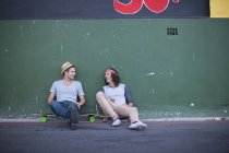 Two adult male friends sitting on skateboards and chatting — Stock Photo