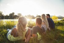 Four young adult friends reclining on riverbank — Stock Photo
