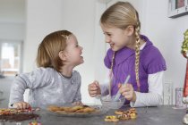 Дівчата на кухонній стійці прикрашають печиво обличчям до обличчя посміхаючись — стокове фото
