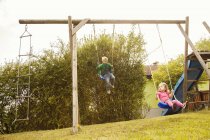 Brother and sister playing on swings in garden — Stock Photo