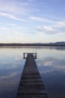 Cais de madeira e céu nublado refletindo na água do lago — Fotografia de Stock