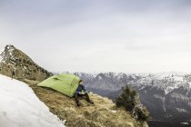 Young male hiker in front of tent on peak of Klammspitze mountain, Oberammergau, Bavaria, Germany — Stock Photo