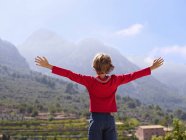 Rear view of boy looking at mountains with arms outstretched, Majorca, Spain — Stock Photo