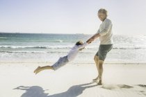 Father swinging son on beach — Stock Photo