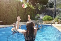 Teenage girl throwing ball to mother and brother in swimming pool — Stock Photo
