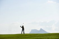 Golfista prendendo golf swing di fronte alla catena montuosa — Foto stock