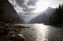 Скелястий берег гірської річки з сонячним світлом, що відображає у воді — стокове фото