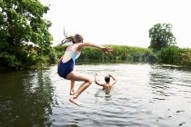 Adolescente chico y hermana saltando en el lago - foto de stock
