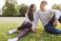 Молода пара сидить на траві обличчям до обличчя посміхаючись — стокове фото