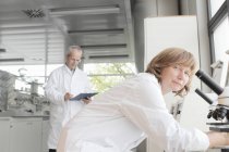 Científicos trabajando en laboratorio, mujer con microscopio y hombre tomando notas - foto de stock