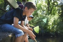 Jungen sitzen auf Mauer und angeln im Flusswasser — Stockfoto