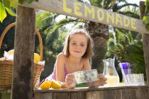Porträt eines Mädchens auf Limonadenständer, das einen Hundert-Dollar-Schein hochhält — Stockfoto