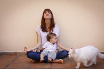 Retrato de mulher adulta média praticando ioga com filha bebê no chão da cozinha — Fotografia de Stock