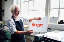 Senior craftsman/technician holding up letterpress print in book arts workshop — Stock Photo