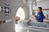 Девушка младшего возраста идет на компьютерную томографию с женщиной-радиографом и мужчиной на заднем плане — стоковое фото