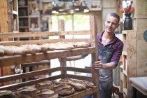 Portrait de jeune boulanger masculin avec étagères de pain frais — Photo de stock