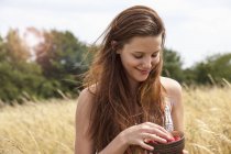 Young woman holding bowl of fresh fruit in field — Stock Photo