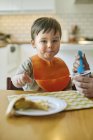 Bébé garçon assis à la table étant nourri yaourt par mère — Photo de stock