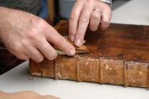 Mãos de encadernador tradicional masculino sênior remoção de couro do livro — Fotografia de Stock