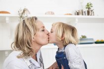 Девушка целует мать на кухне — стоковое фото