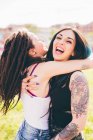 Татуйовані молоді жінки сміються і обіймаються в міському парку — стокове фото