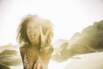 Donna felice mostrando segno di pace sulla spiaggia — Foto stock
