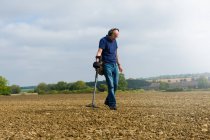 Зрелый человек в наушниках ищет грязное поле с помощью металлоискателя — стоковое фото